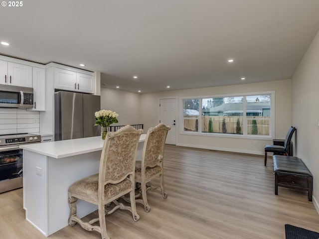 kitchen featuring white cabinetry, stainless steel appliances, light hardwood / wood-style floors, backsplash, and a breakfast bar