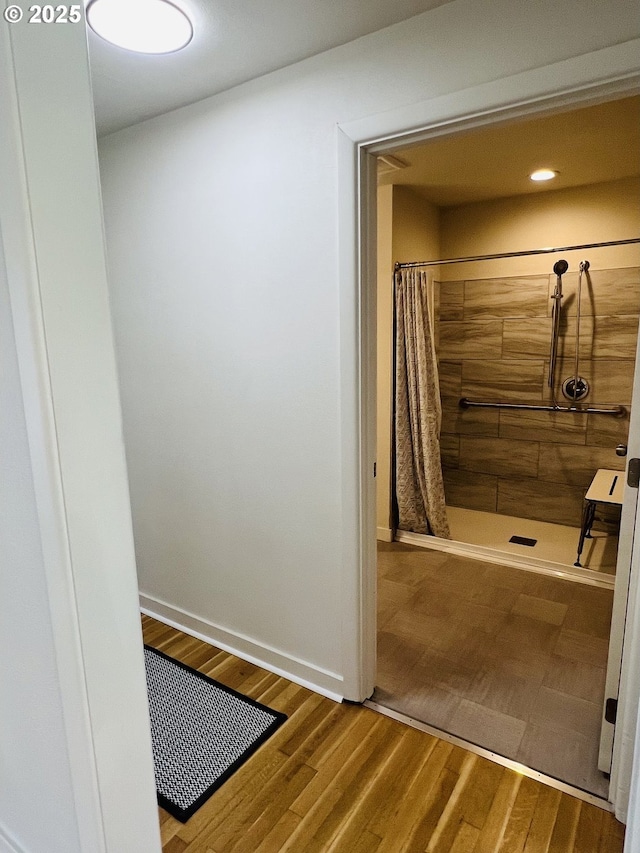 bathroom with recessed lighting, baseboards, wood finished floors, and a tile shower