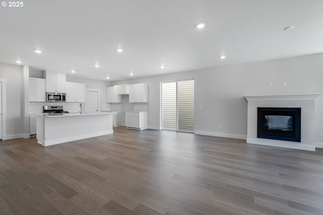 unfurnished living room with a sink, baseboards, recessed lighting, a fireplace, and dark wood-type flooring