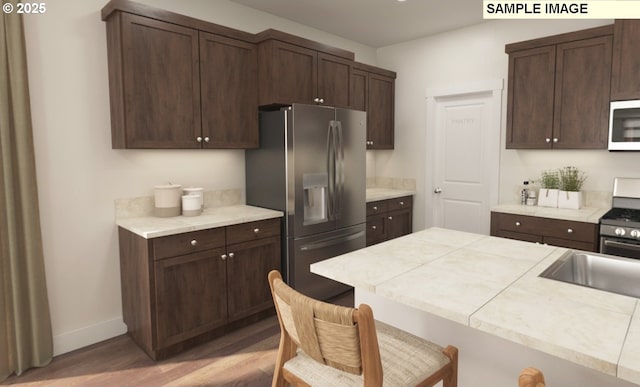 kitchen with a kitchen bar, light wood-style floors, appliances with stainless steel finishes, light countertops, and dark brown cabinets