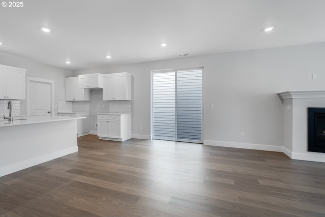 unfurnished living room featuring baseboards, a sink, and dark wood-style flooring