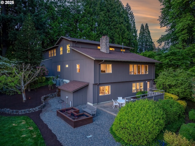 back of property at dusk with a chimney, a patio, central air condition unit, and roof with shingles