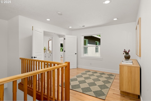 corridor with light wood-type flooring, recessed lighting, an upstairs landing, baseboards, and a textured ceiling