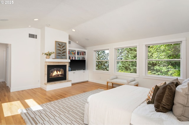 bedroom with multiple windows, a glass covered fireplace, lofted ceiling, light wood-style flooring, and baseboards