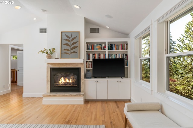 living area featuring light wood finished floors, a glass covered fireplace, recessed lighting, and high vaulted ceiling