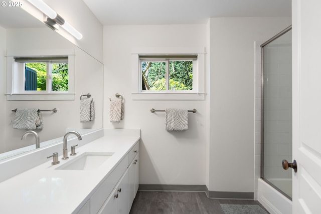 full bathroom featuring healthy amount of natural light, vanity, baseboards, and bath / shower combo with glass door