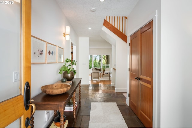 hall with stone tile flooring, recessed lighting, a textured ceiling, and baseboards