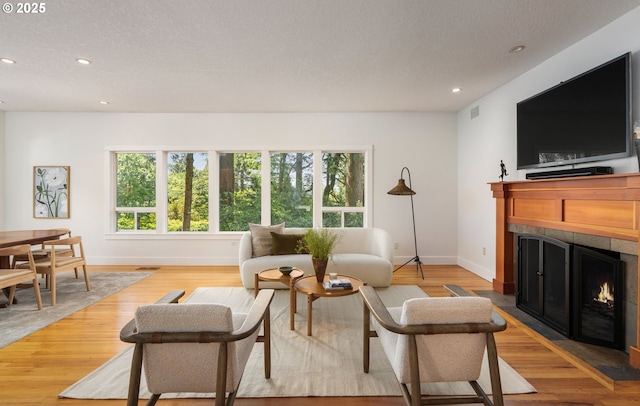 living room featuring a tiled fireplace, baseboards, recessed lighting, light wood-style flooring, and a textured ceiling