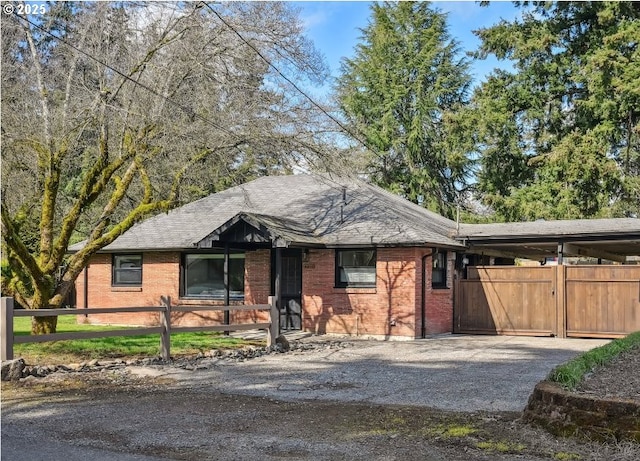 single story home featuring aphalt driveway, an attached carport, roof with shingles, brick siding, and a fenced front yard