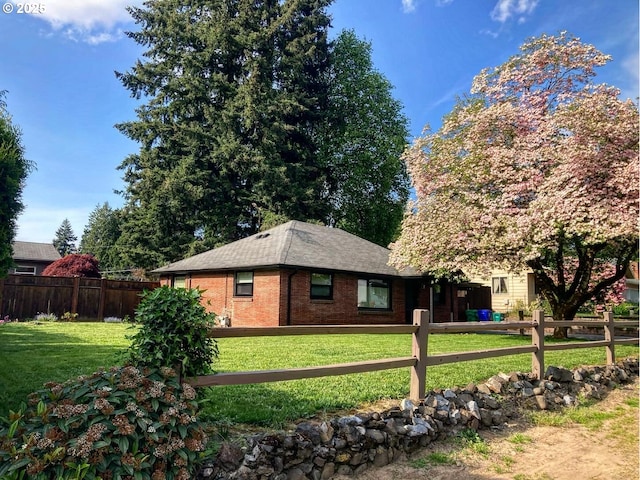 view of property exterior with fence, a yard, a shingled roof, and brick siding