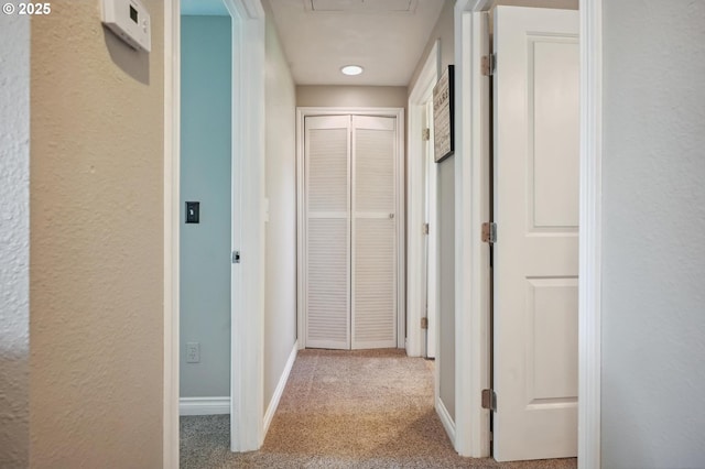 hall featuring baseboards, attic access, carpet, and a textured wall