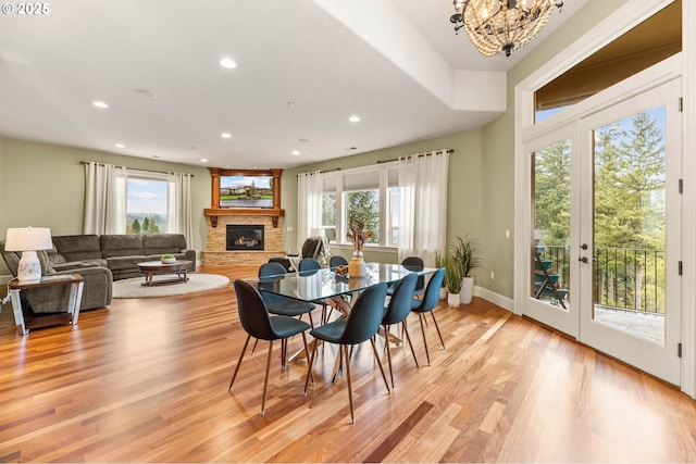 dining room with a stone fireplace, recessed lighting, a healthy amount of sunlight, and light wood-type flooring