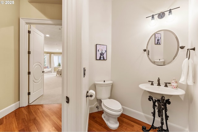 half bathroom with baseboards, wood finished floors, and toilet