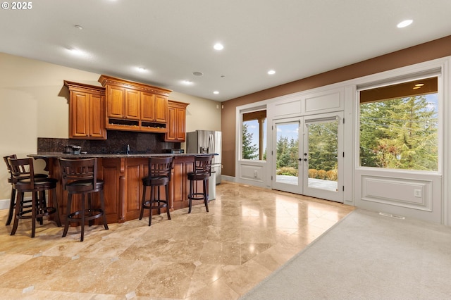 kitchen with stainless steel refrigerator with ice dispenser, a wealth of natural light, a breakfast bar, and backsplash