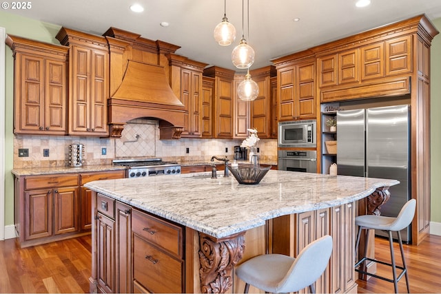 kitchen featuring a breakfast bar, custom exhaust hood, hanging light fixtures, a large island with sink, and stainless steel appliances