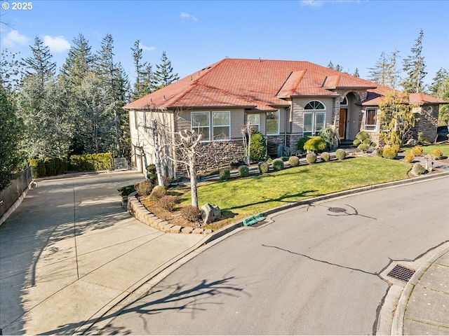 view of front of house featuring fence, stone siding, a front yard, a tiled roof, and driveway
