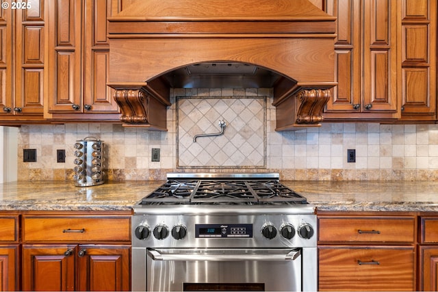 kitchen with brown cabinets, stainless steel range, light stone countertops, and tasteful backsplash