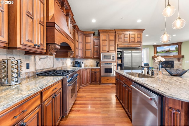 kitchen with brown cabinets, appliances with stainless steel finishes, a sink, and premium range hood