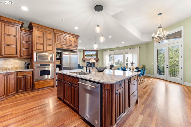 kitchen featuring pendant lighting, sink, appliances with stainless steel finishes, a kitchen island with sink, and light stone counters