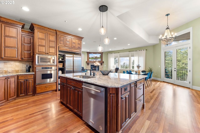 kitchen with stainless steel appliances, a notable chandelier, a sink, and light wood-type flooring