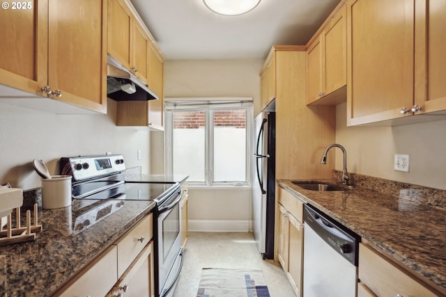 kitchen featuring appliances with stainless steel finishes, a sink, under cabinet range hood, light brown cabinets, and dark stone counters