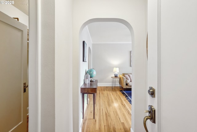 corridor with light wood-style flooring, arched walkways, ornamental molding, and baseboards