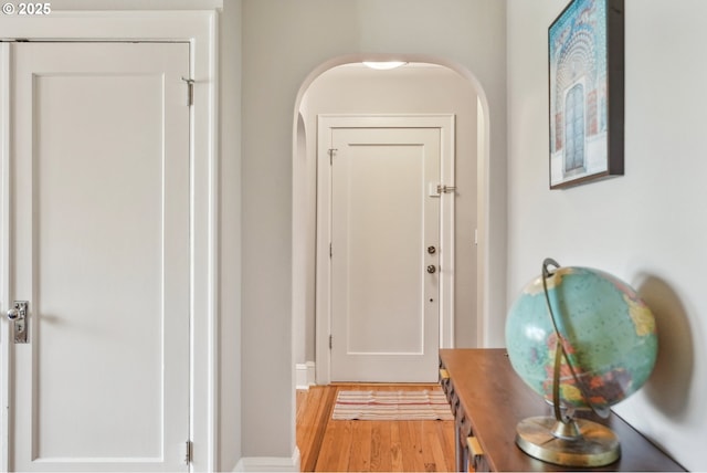 corridor with light wood-style floors, arched walkways, and baseboards