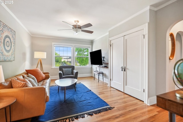 living room with light wood-style floors, a ceiling fan, crown molding, and baseboards
