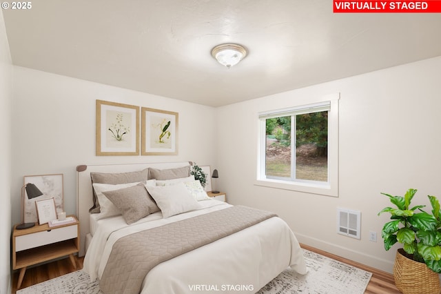 bedroom with baseboards, visible vents, and wood finished floors