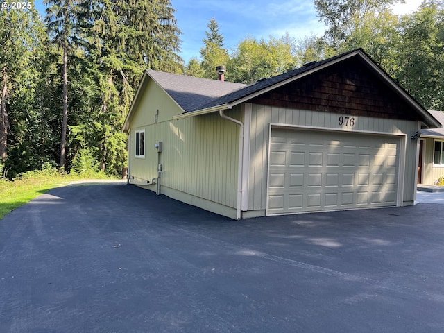 view of home's exterior with an attached garage, a shingled roof, and aphalt driveway