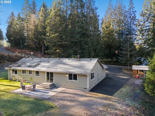 rear view of property featuring crawl space, a patio area, a lawn, and roof with shingles