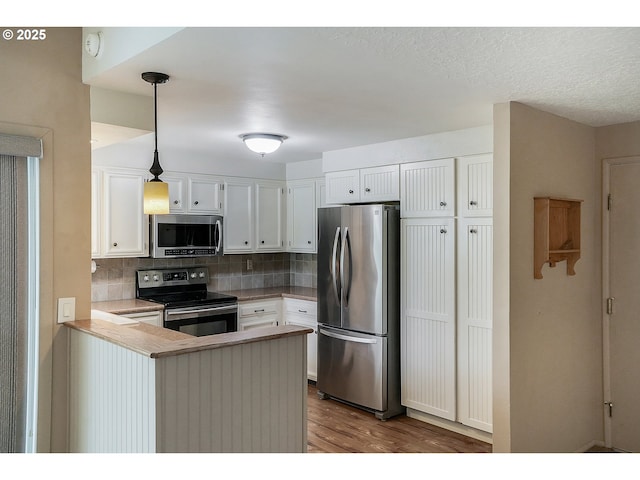 kitchen featuring white cabinets, dark wood-style flooring, stainless steel appliances, a peninsula, and backsplash