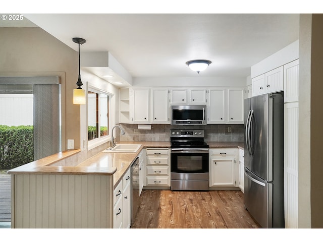 kitchen with white cabinets, appliances with stainless steel finishes, a sink, a peninsula, and wood finished floors