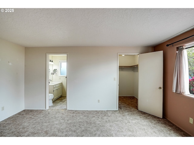 unfurnished bedroom featuring light carpet, a sink, a textured ceiling, ensuite bathroom, and a spacious closet