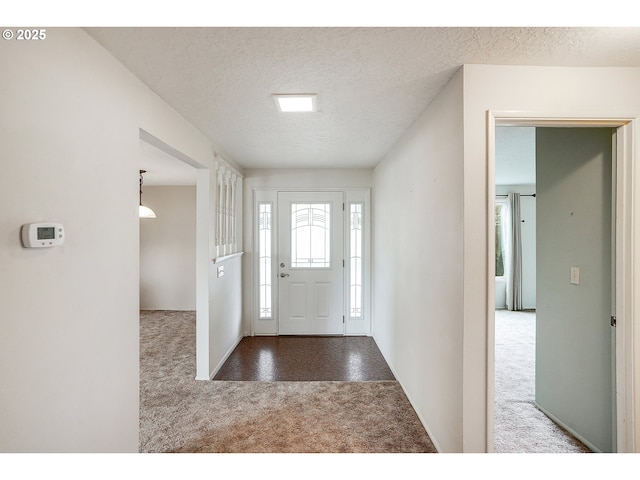 foyer featuring a textured ceiling, baseboards, and carpet