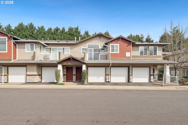 view of front facade with an attached garage, driveway, a balcony, and stone siding