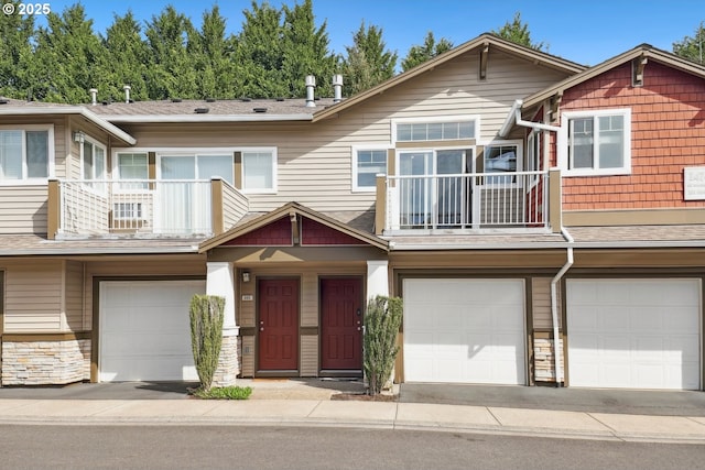 townhome / multi-family property featuring a garage, stone siding, driveway, and a balcony
