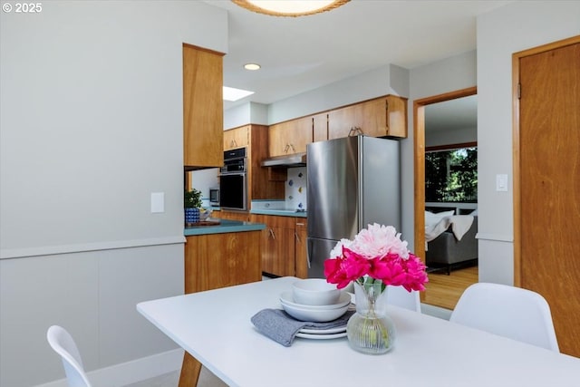 15 SW 95th Ave, Portland, OR 97225 - kitchen with freestanding refrigerator, oven, under cabinet range hood, brown cabinetry, and cooktop