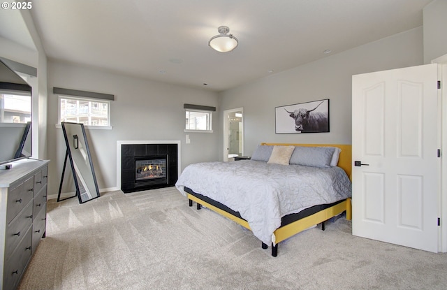 bedroom featuring baseboards, a tile fireplace, and light colored carpet