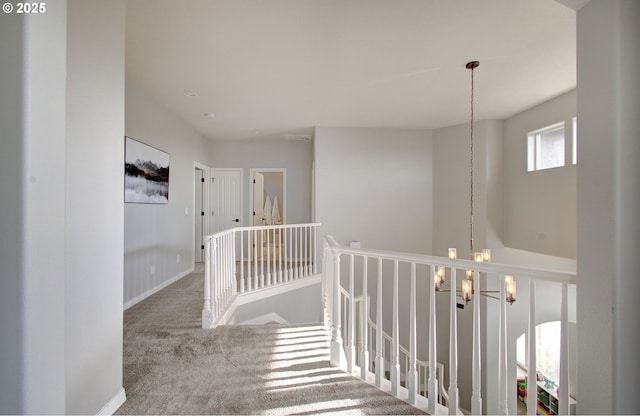 corridor featuring baseboards, carpet, an upstairs landing, and an inviting chandelier