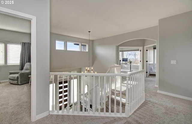 corridor with light carpet, a healthy amount of sunlight, baseboards, and an inviting chandelier