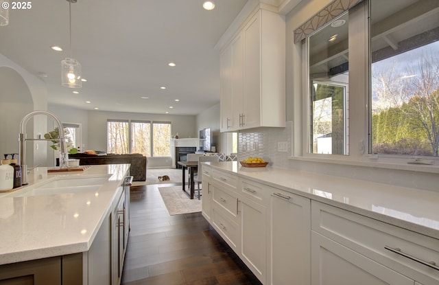 kitchen featuring light stone counters, a sink, white cabinets, open floor plan, and hanging light fixtures