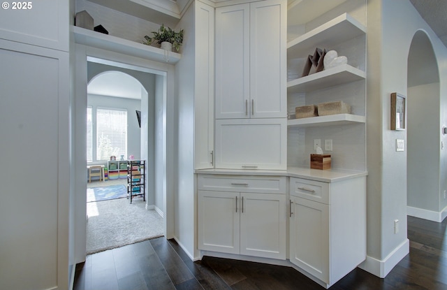 bar with dark carpet, baseboards, arched walkways, and dark wood finished floors