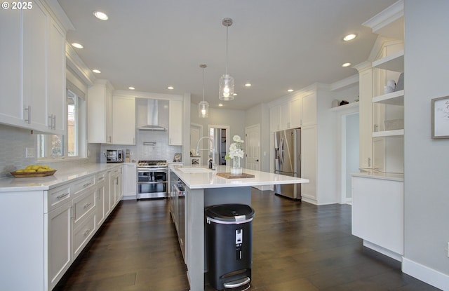 kitchen featuring stainless steel appliances, a sink, white cabinets, wall chimney range hood, and an island with sink