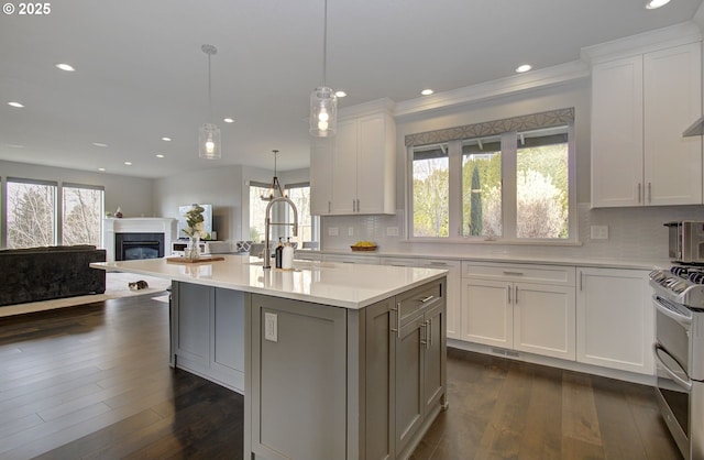 kitchen featuring range with two ovens, pendant lighting, light countertops, a kitchen island with sink, and white cabinets