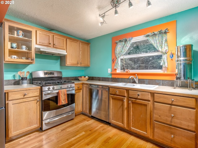 3843 SE 41st Ave SE, Portland, OR 97202 - kitchen featuring appliances with stainless steel finishes, under cabinet range hood, light wood-style flooring, a textured ceiling, and glass insert cabinets