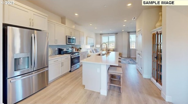 7510 NW Elise Ave, Portland, OR 97229 - kitchen featuring appliances with stainless steel finishes, a kitchen island with sink, tasteful backsplash, light countertops, and light wood-style flooring