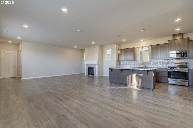 kitchen featuring a kitchen island, open floor plan, decorative backsplash, appliances with stainless steel finishes, and a kitchen breakfast bar