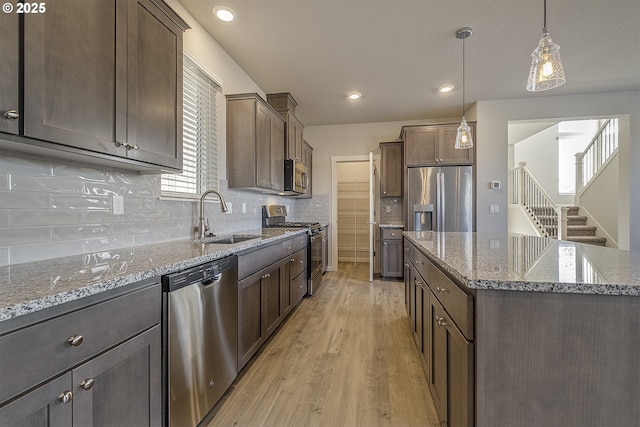 kitchen with tasteful backsplash, light stone counters, light wood-style floors, stainless steel appliances, and a sink