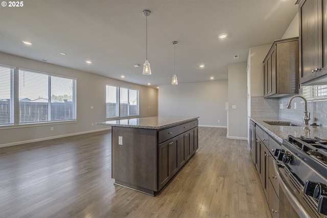 kitchen featuring stainless steel gas range oven, tasteful backsplash, a kitchen island, wood finished floors, and a sink